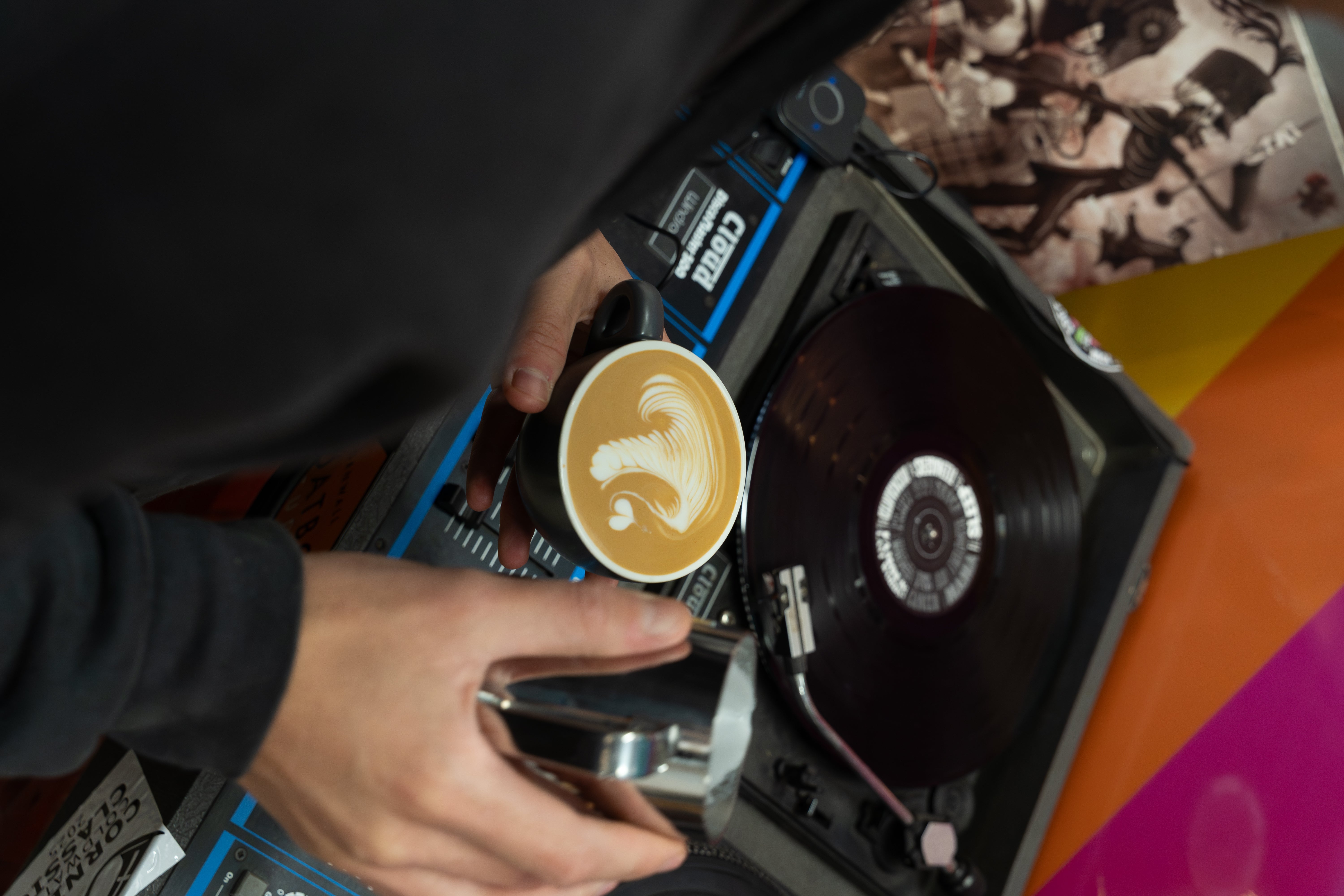 Person holding a cup of coffee with a question mark design next to a record player.